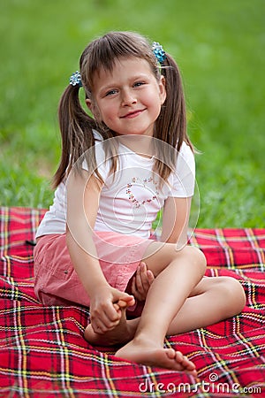 Smiling girl preschooler sitting on plaid in park