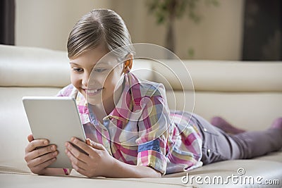 Smiling girl using tablet PC while lying on sofa at home