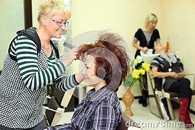 Smiling hairdresser makes hair styling for woman