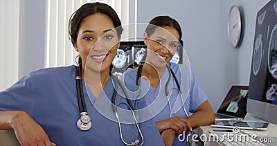 Smiling Hispanic and African American nurses sitting at computer station