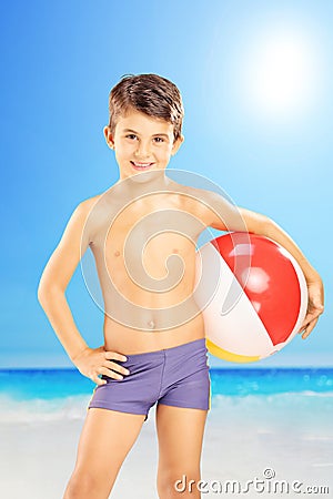 Smiling kid in swimming shorts, holding a beach ball and posing