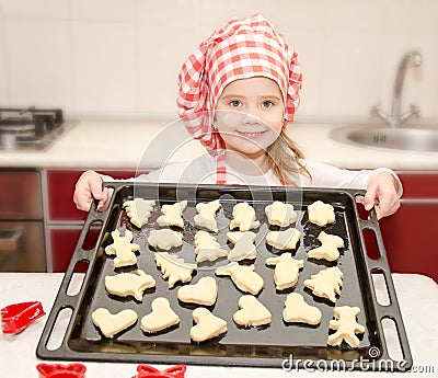 Smiling little girl in chef hat with baking sheet of cookies