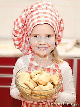 Smiling little girl in chef hat holding bowl with cookies