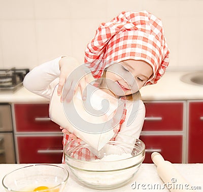 Smiling little girl with chef hat put flour for baking cookies