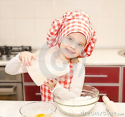 Smiling little girl with chef hat put flour for baking cookies