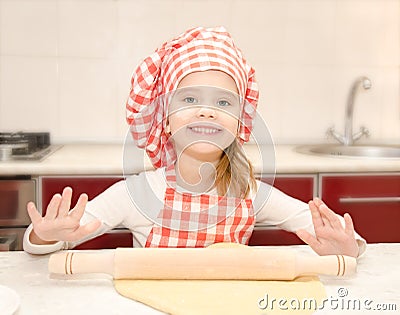 Smiling little girl with chef hat rolling dough