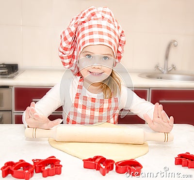 Smiling little girl with chef hat rolling dough