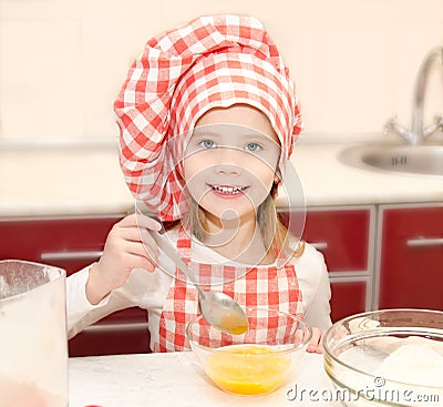 Smiling little girl with chef hat stirrring cookie dough