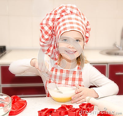 Smiling little girl with chef hat stirrring cookie dough