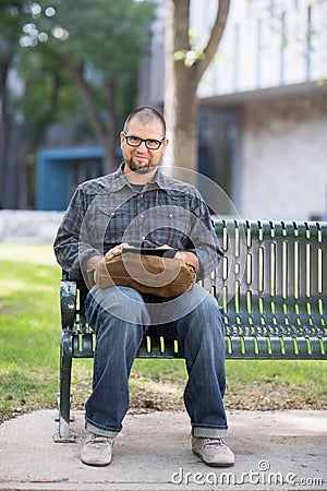 Smiling Male University Student Sitting On Bench