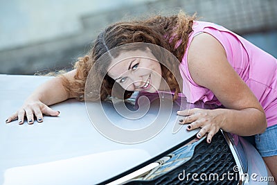 Smiling pretty woman embracing car bonnet with hands
