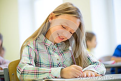 Smiling school girl writing test in classroom