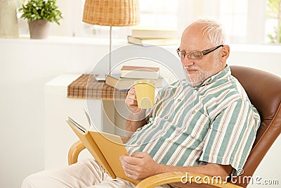 Smiling senior relaxing at home with book and tea