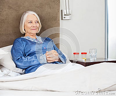 Smiling Senior Woman Relaxing On Bed At Nursing