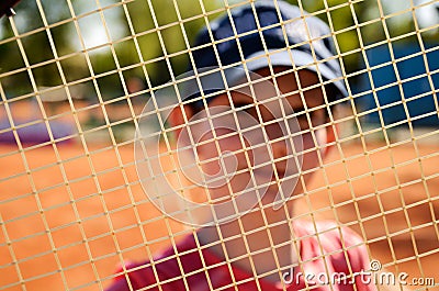 Smiling teenage girl looking through the net of a tennis racket