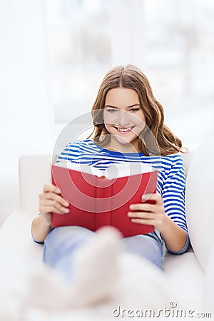 Smiling teenage girl reading book on couch