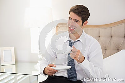 Smiling well dressed man with a cup of tea in bed