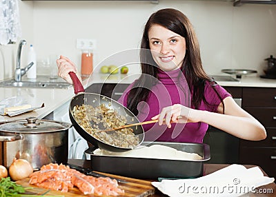 Smiling woman cooking fish pie with salmon and vegetables