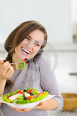 Smiling woman eating salad and talking mobile phone