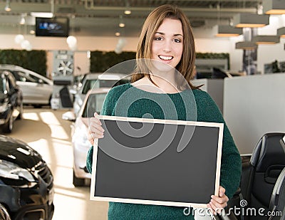 Smiling woman holding blackboard inside car dealership