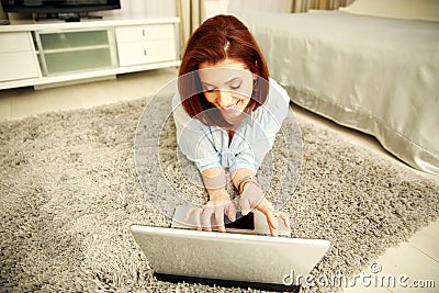 Smiling woman lying on the carpet and typing on the laptop