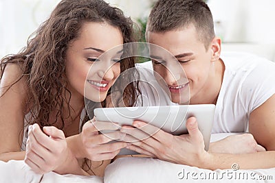 Smiling young couple lying in the bed and use tablet pc