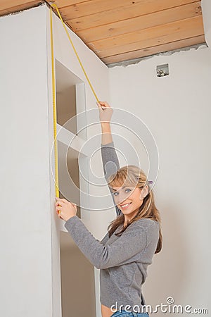 Smiling young girl measuring wall with tape measure