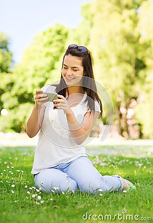 Smiling young girl with smartphone sitting in park