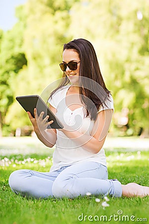 Smiling young girl with tablet pc sitting on grass