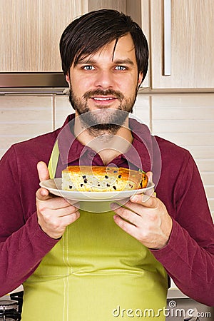 Smiling young man with apron holding a plate with homemade cake