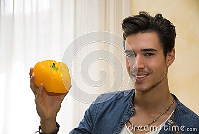 Smiling young man holding a fresh yellow pepper or capsicum in his hand