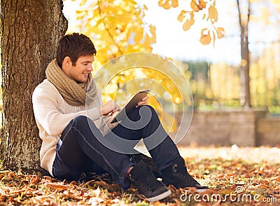 Smiling young man with tablet pc in autumn park