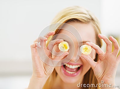 Smiling young woman holding banana slices in front of eyes