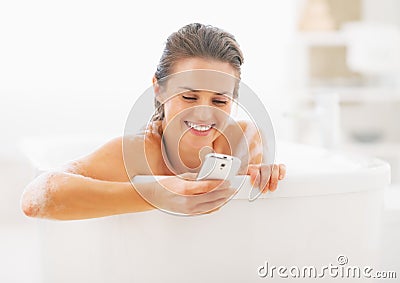 Smiling young woman writing sms in bathtub