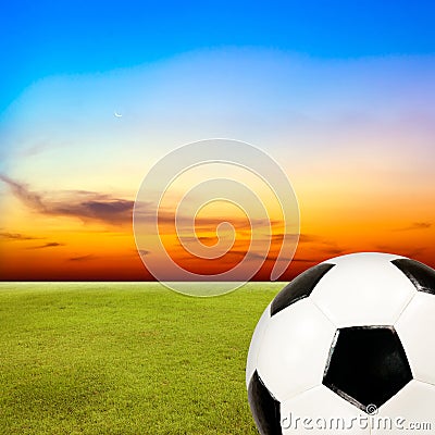 Soccer ball with green grass field against sunset sky