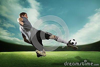 Soccer player kicking the soccer ball in mid air, in the stadium with the sky