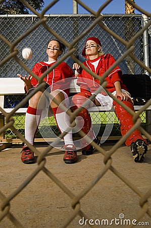 Softball players sitting on bench, front view.