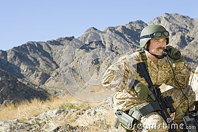 Soldier Using Telephone While Holding Rifle Against Mountain