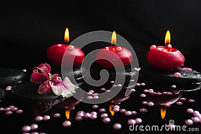 Spa still life of red candles, zen stones with drops, orchid