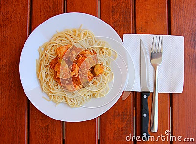 Spaghetti with chicken meat, vegetable marrow and red sauce on a white plate.