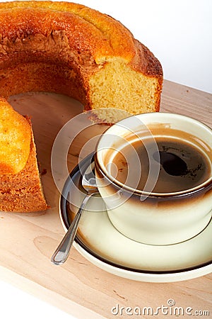 Sponge cake with the cup of coffee and spoon on wood plate