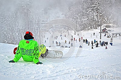 Sportsman in green suite with skateboard seating on snow,