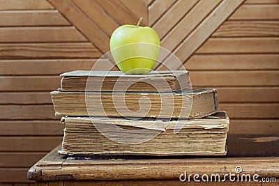 Stack of old books and green apple on old chair