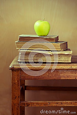 Stack of old books and green apple on old chair