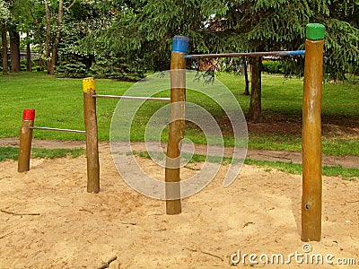 Steel horizontal bars on wooden pillars in children playground. Orange sand below bars