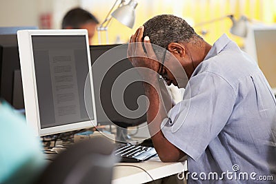 Stressed Man Working At Desk In Busy Creative Office