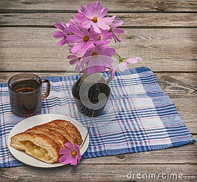 Strudel with apples and a cup of tea next to a bouquet of cosmos