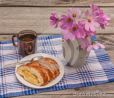 Strudel with apples and a cup of tea next to a bouquet of cosmos