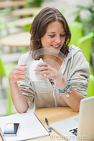 Student drinking coffee while using laptop at cafeteria table