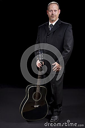 Successful business man in suit standing with guitar on black background